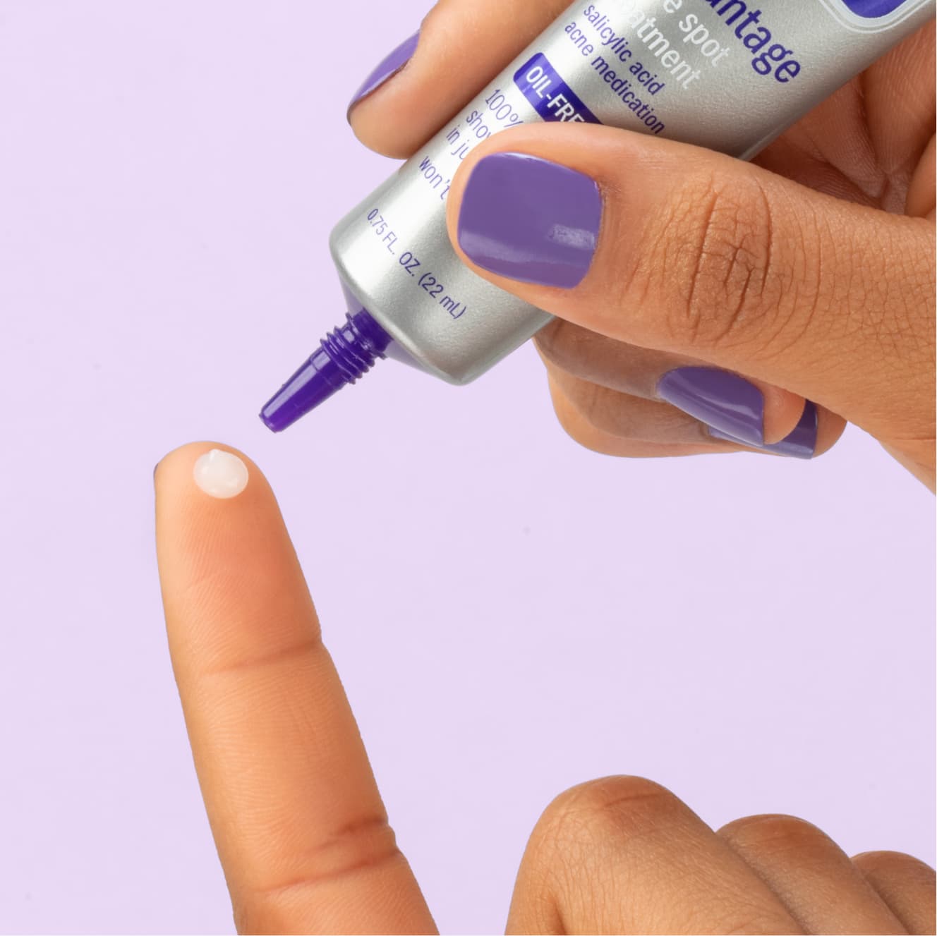 White Advantage spot treatment being applied by hand with purple nails on index finger 