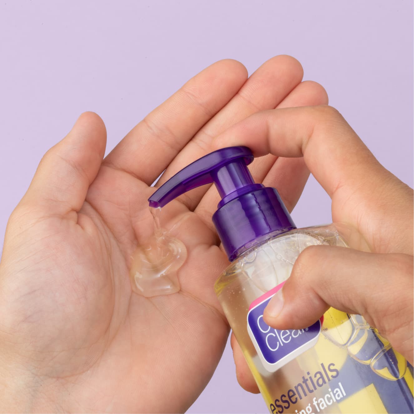 Clear Clean & Clear foaming facial cleanser for sensitive skin being pumped into palm of hand in front of purple background