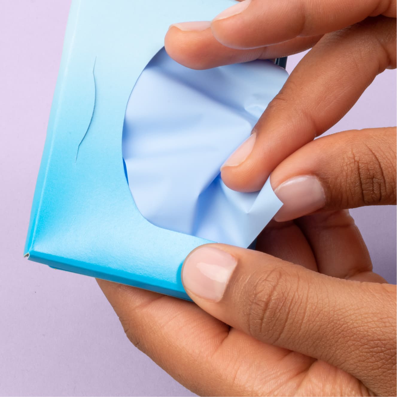 Hand pulls out a single oil absorbing sheet from light blue packet of Clean & Clear oil absorbing sheets container