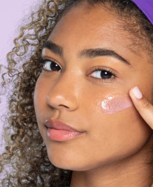 teen with purple headband applying gel moisturizer to cheeks