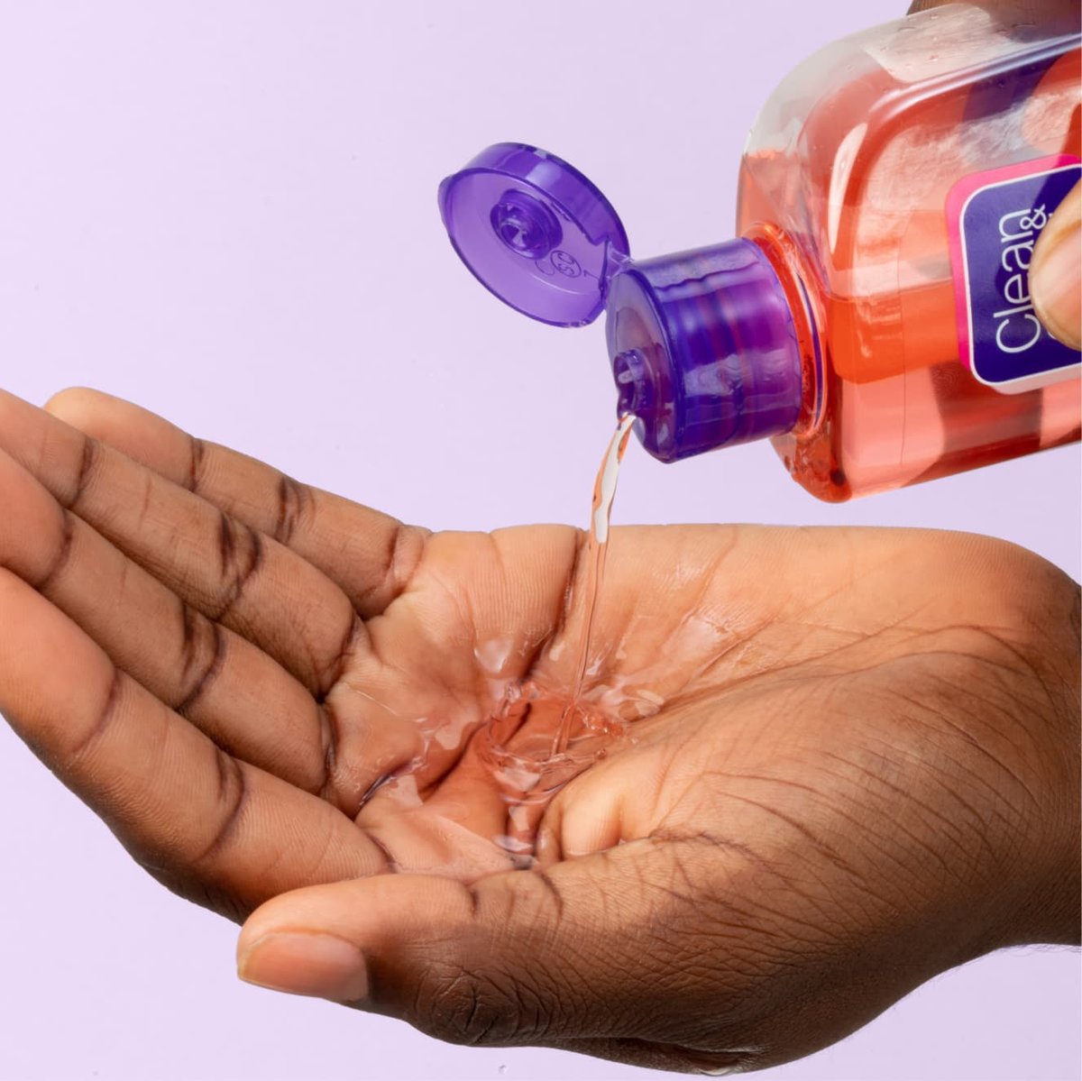 Pink Clean & Clear deep cleaning astringent gel squeezed into palm of hand in front of light purple background