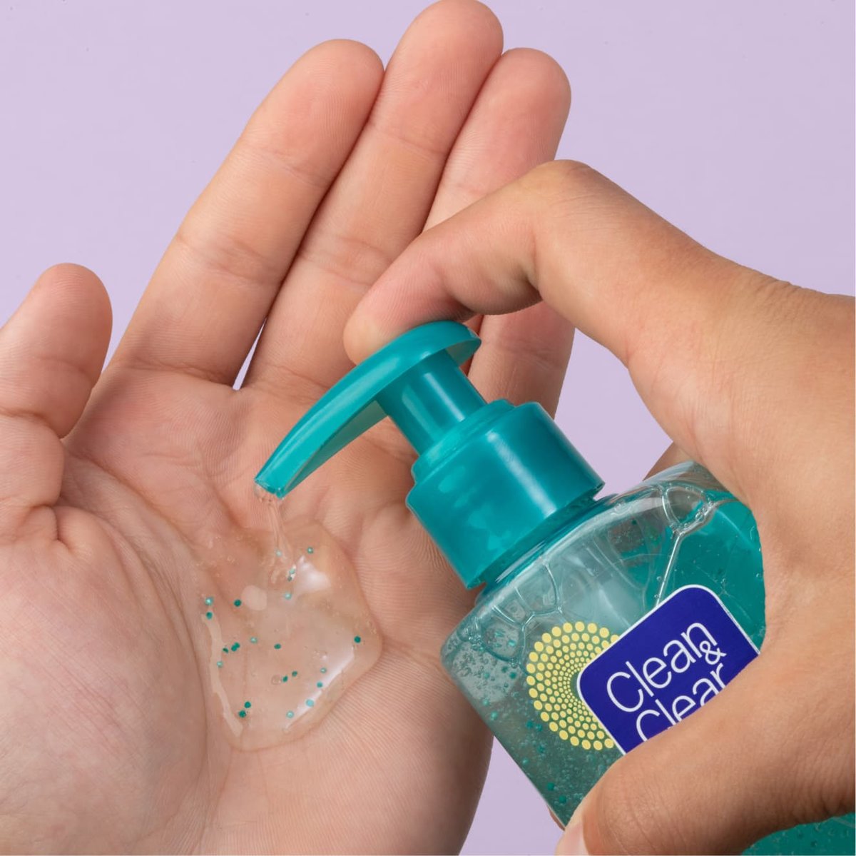 Clear with blue beads Clean & Clear Morning Burst hydrating facial cleanser being pumped into palm of hand in front of purple background