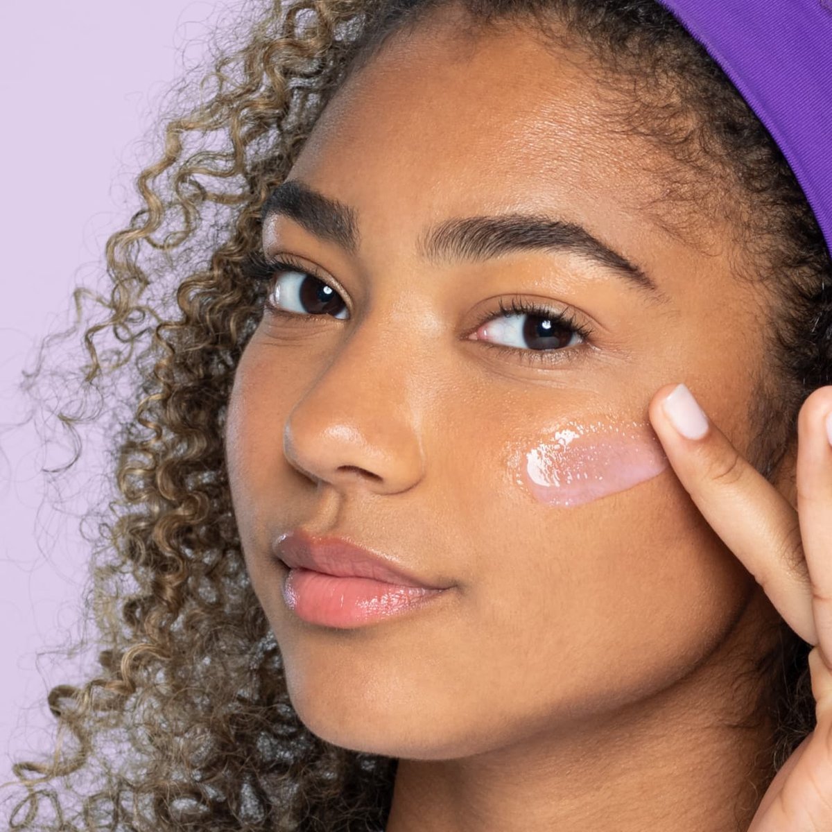 Young teen with brown eyes and curly brown hair with purple headband applies watermelon gel moisturizer with finger onto cheek
