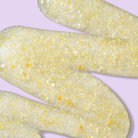 Yellow squiggle of lemon zesty scrub with orange beads in front of light purple background